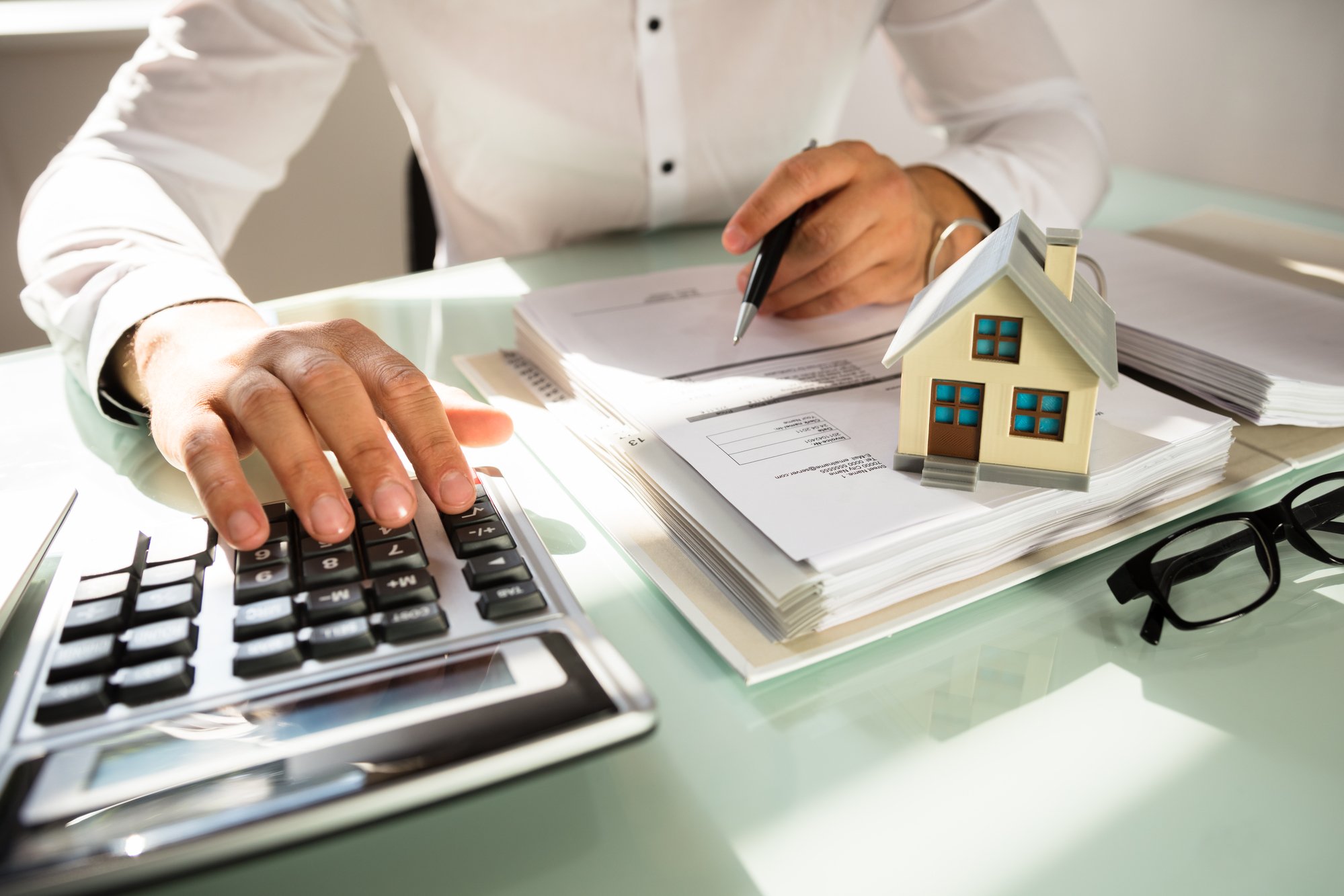 Businessman's hand calculating invoice with house model in office