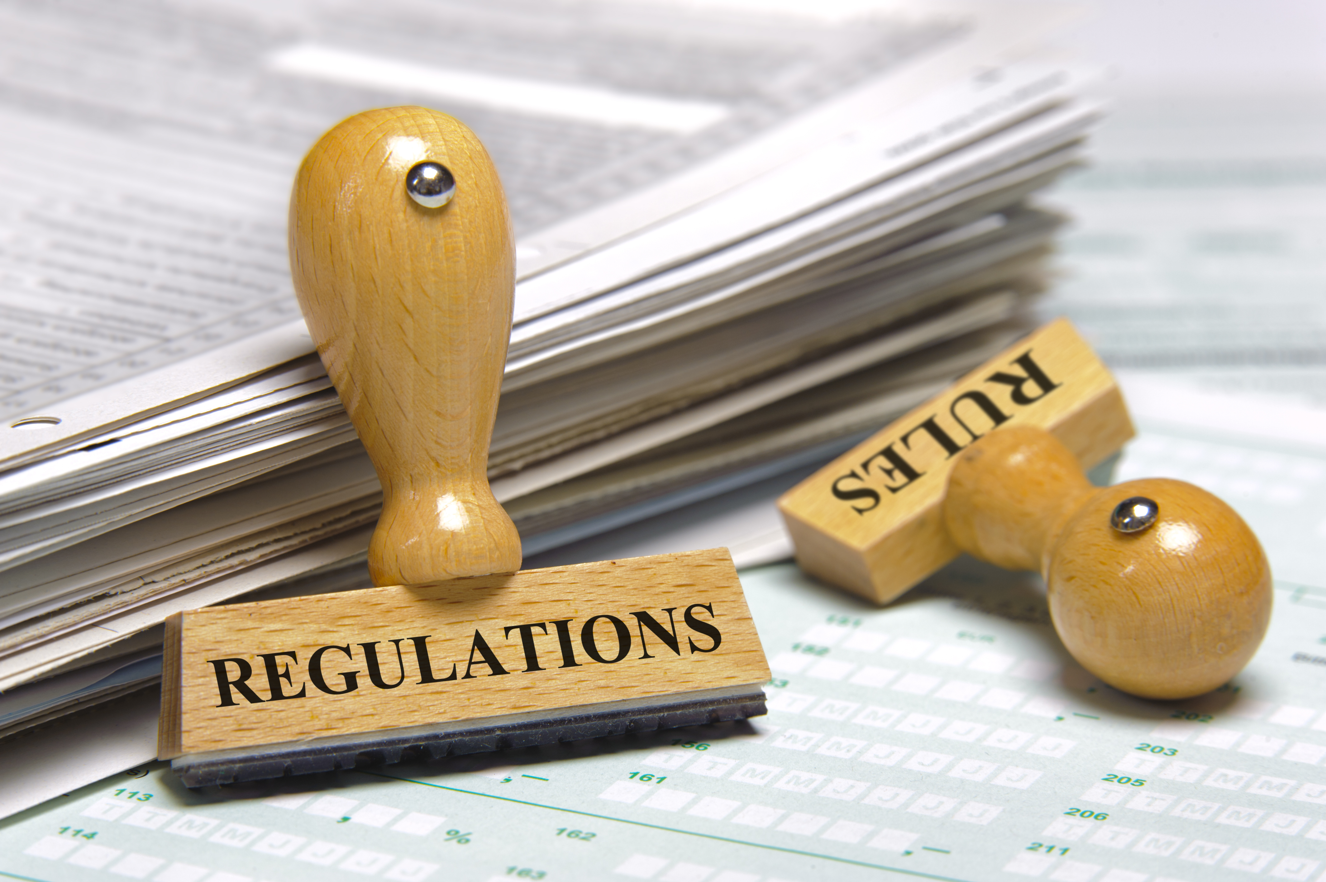 Image of a stack of papers and rubber stamps marked with "Regulations" and "rules" symbolizing land use and zoning laws. 
