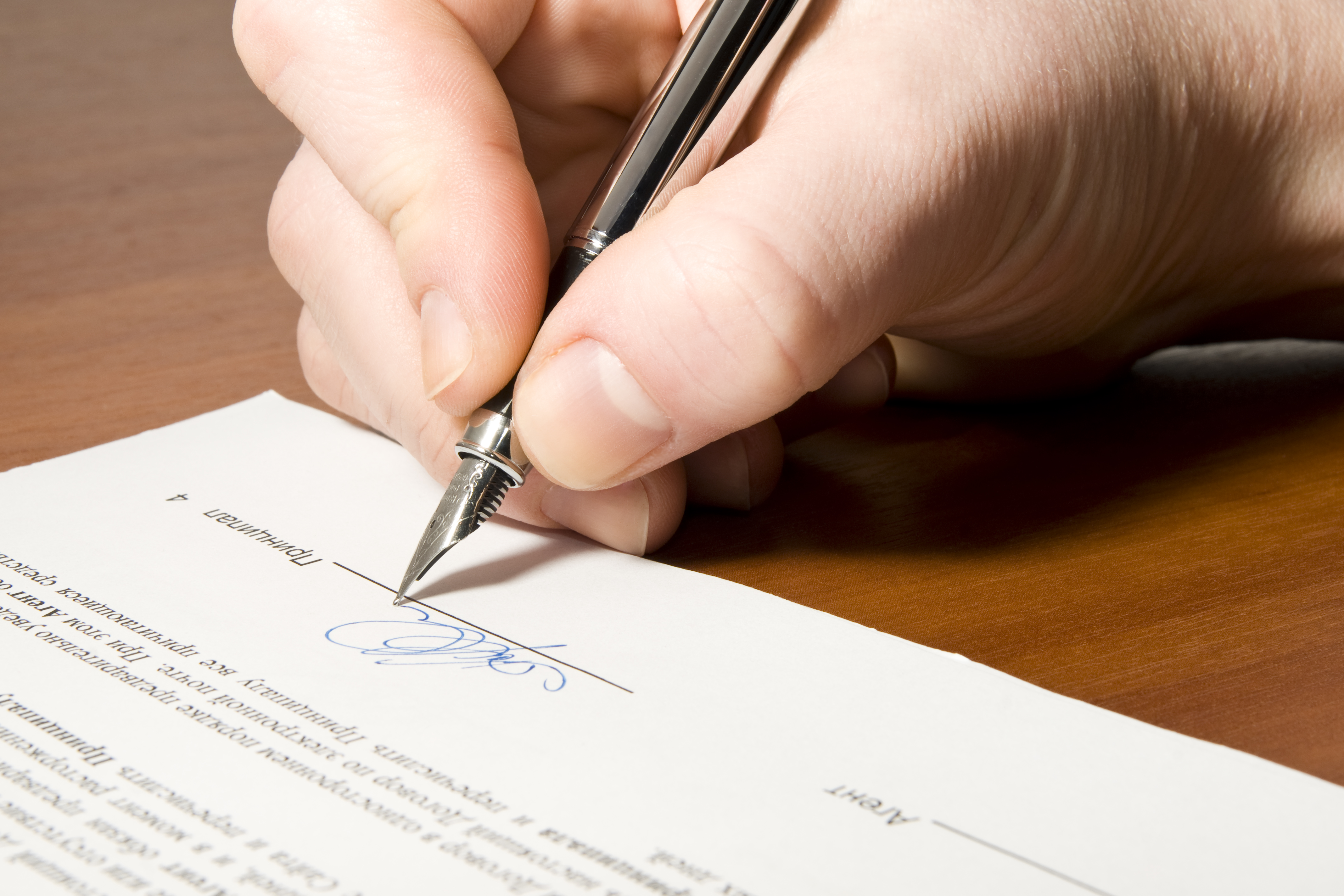 Close up of the hand holding the pen and signing the contract