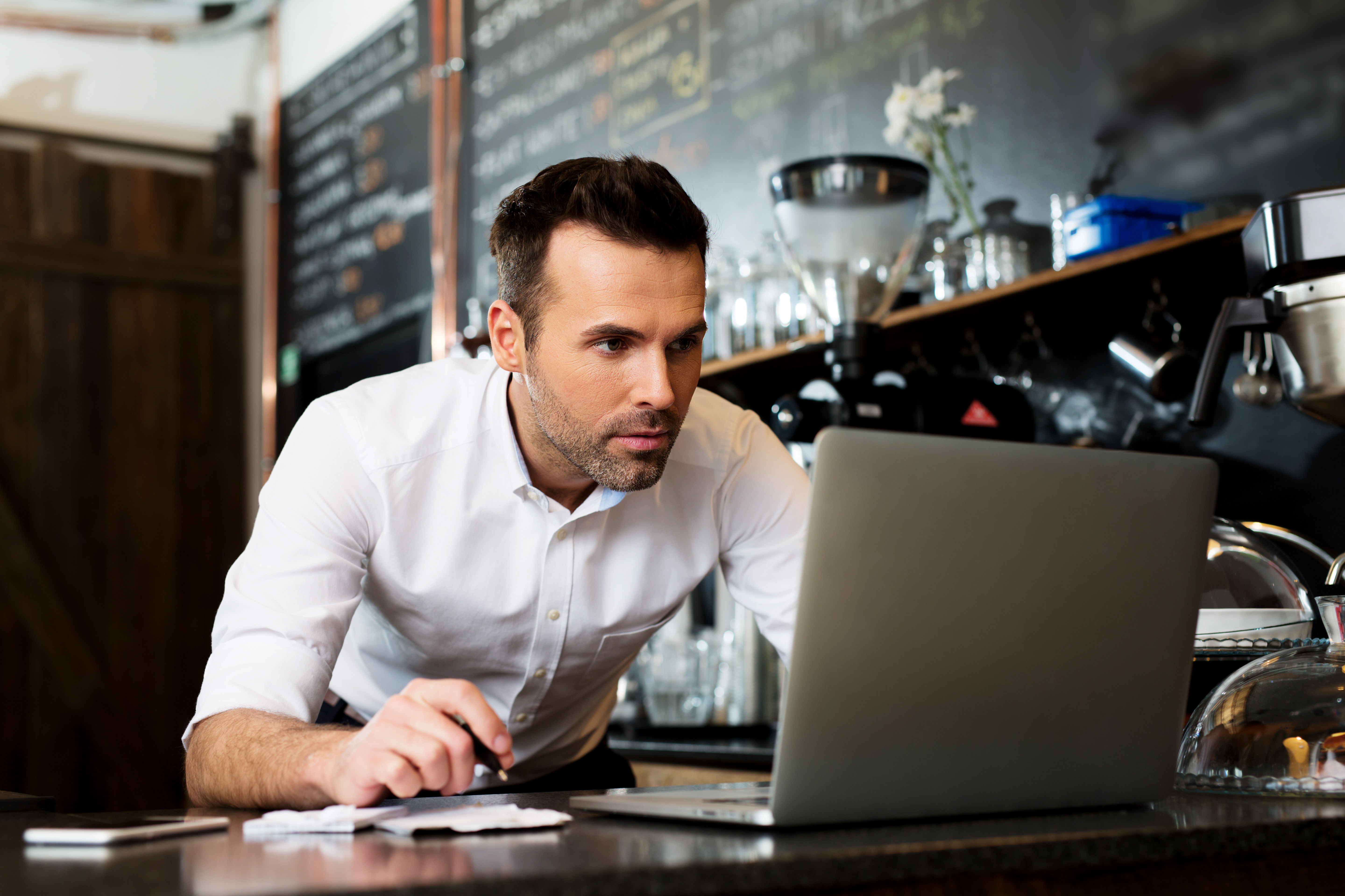 Male business owner crouched over a computer at his restaurant doing work. 