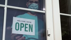 Close up of a male Caucasian with a mask turning a signboard on the glass door of the shop from CLOSED to OPEN. Reopening of a small business activity after quarantine covid-19 emergency.