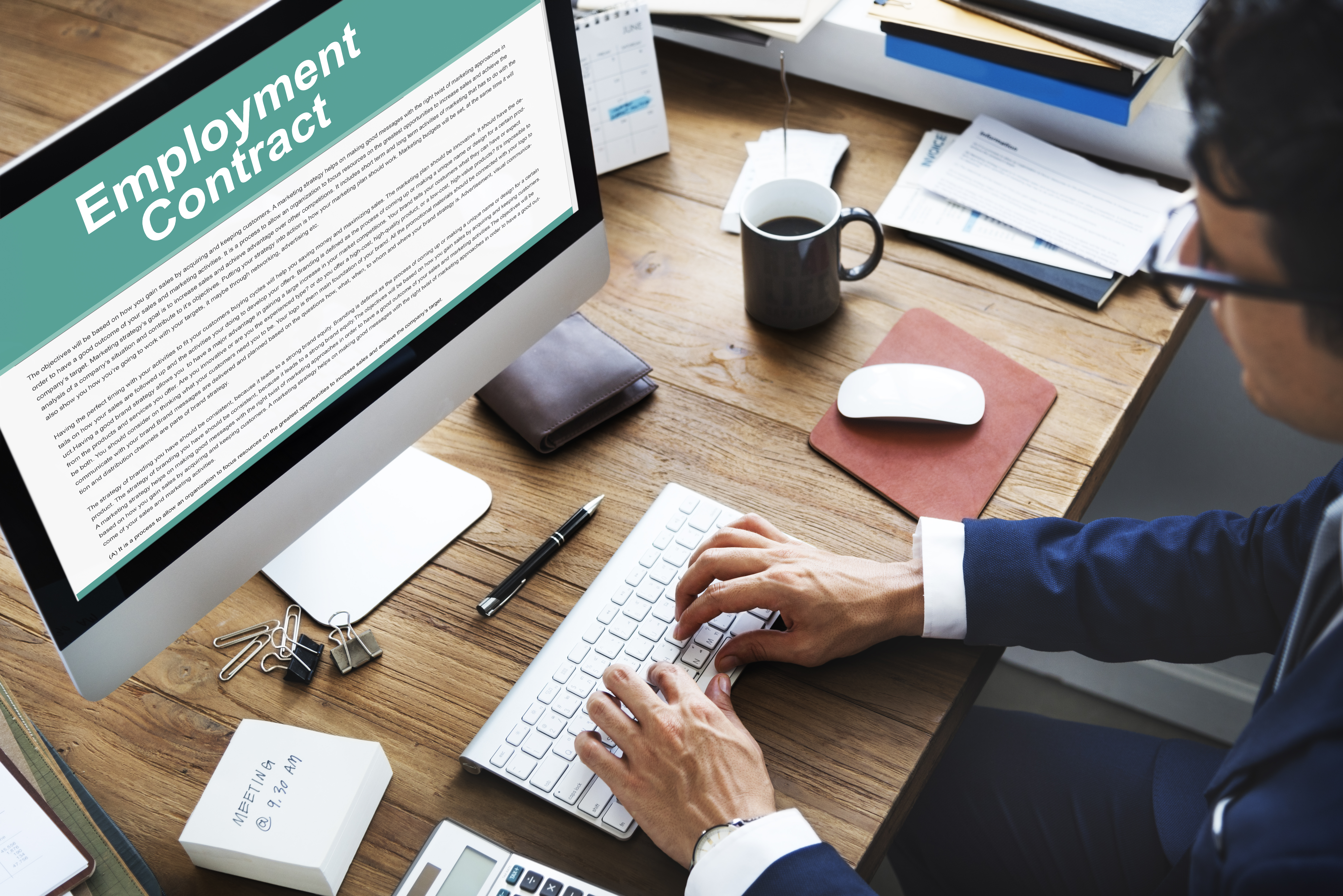 Man's hands typing on keyboard on a crowded desk with a computer monitor that says 'employment contract' to symbolize employment law updates in DC. 