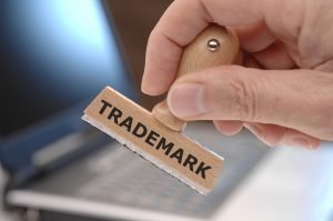 Image of a person's hand holding a rubber stamp that says "Trademark" representing protecting you business through trademark law. 