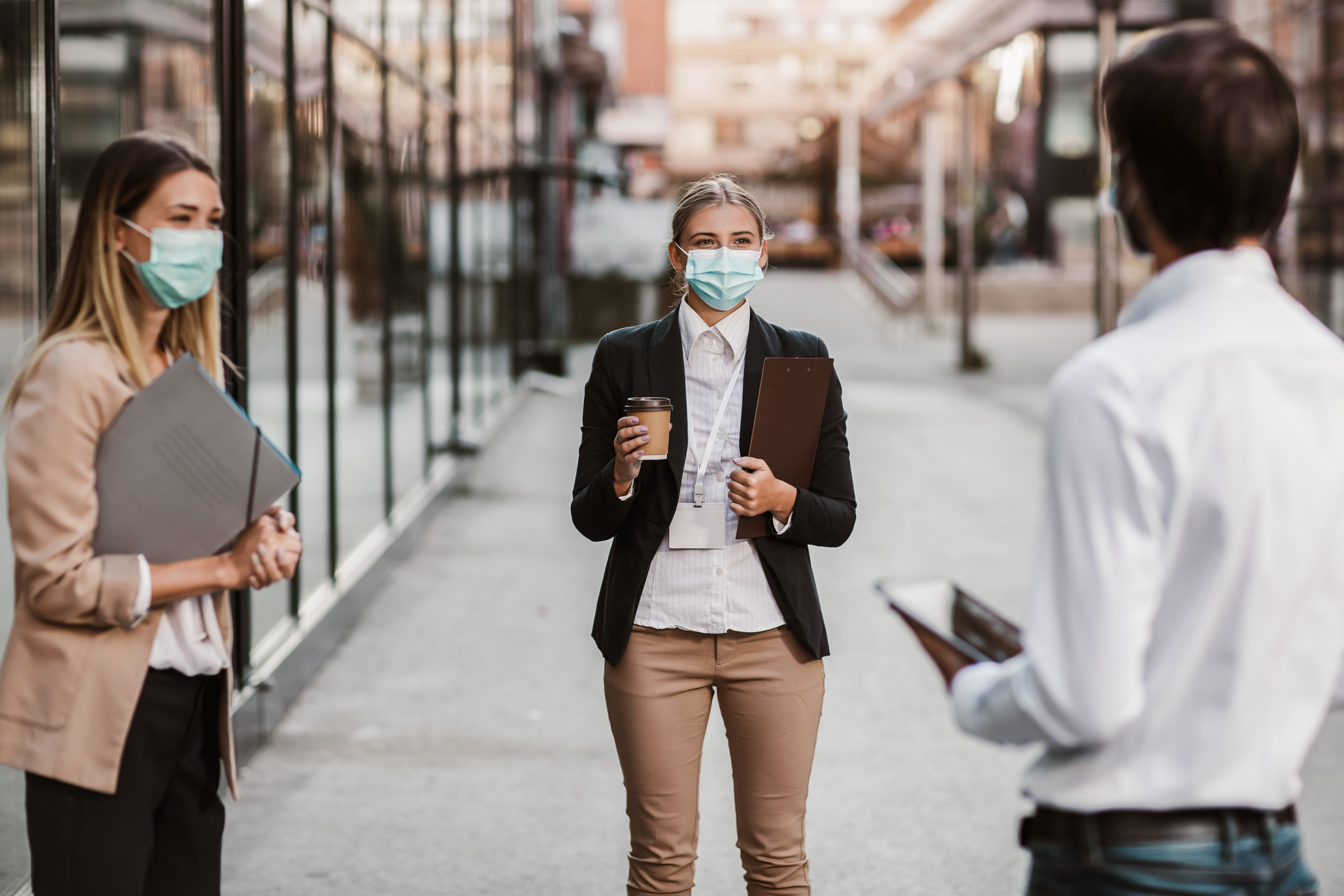 Three employers standing in social distance wearing face mask looking at each other and talking