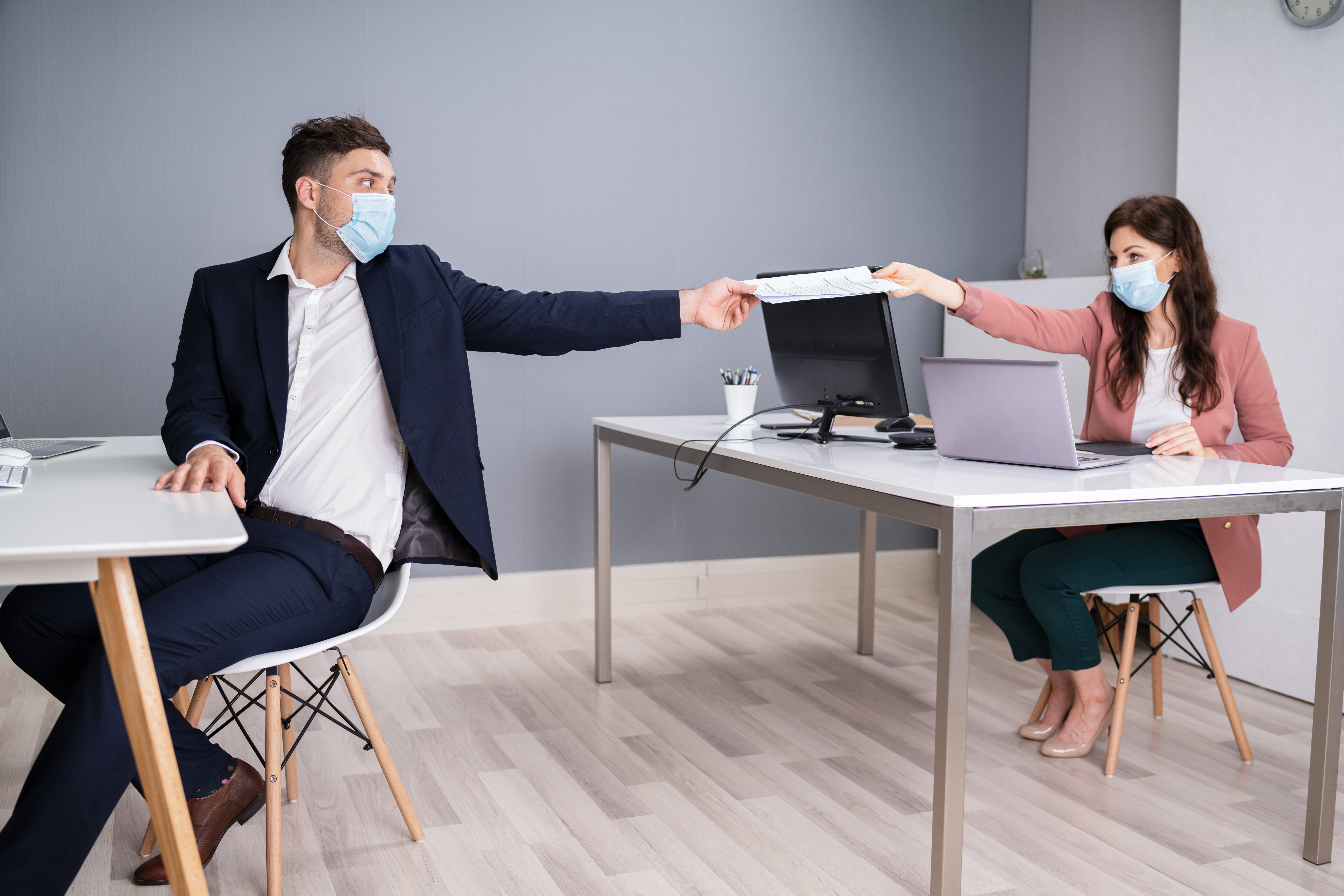 Man and a woman at an office working with masks on and social distancing. 