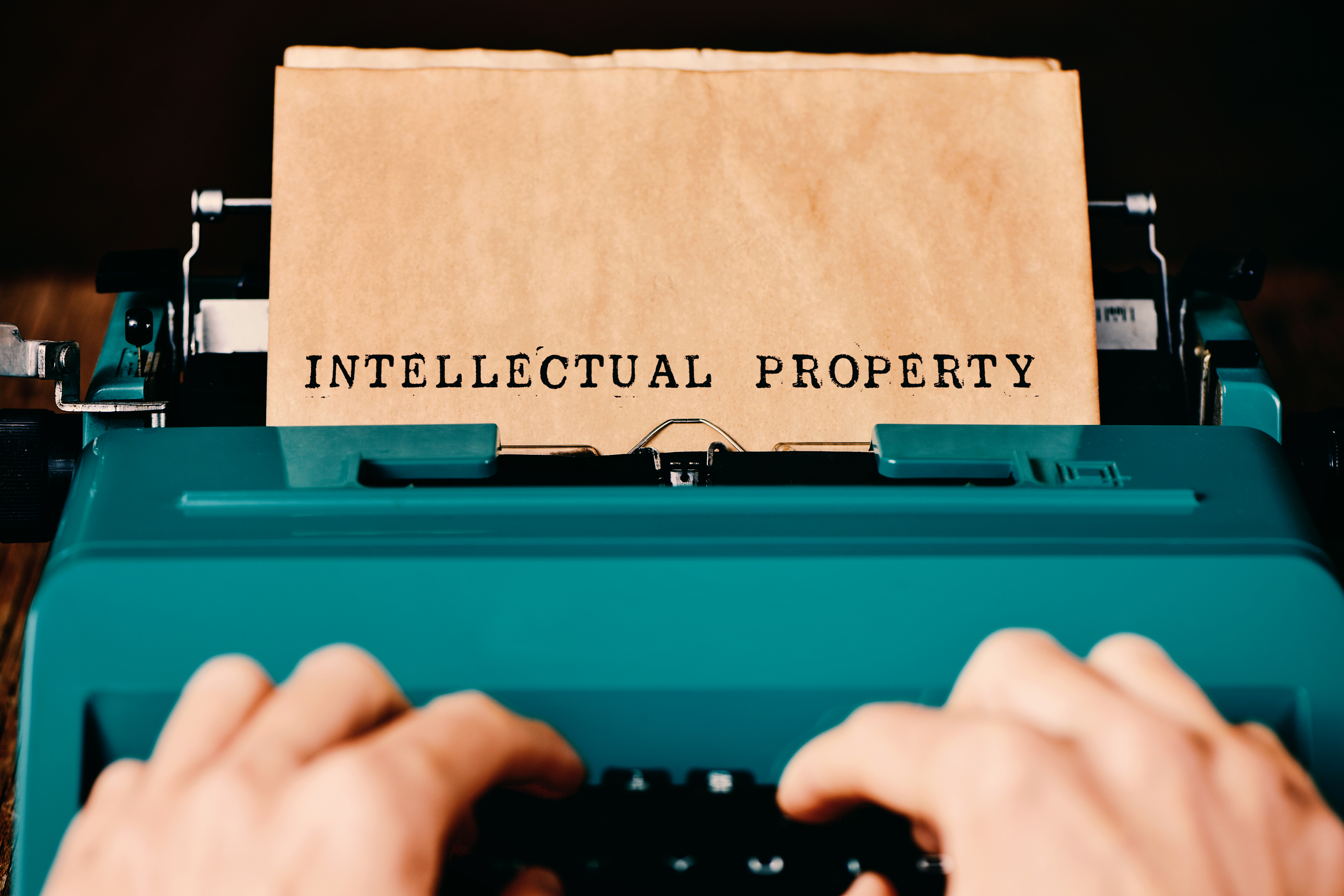 Image of hands typing "Intellectual Property" on a teal typewriter representing IP law or Intellectual Property lawyers. 