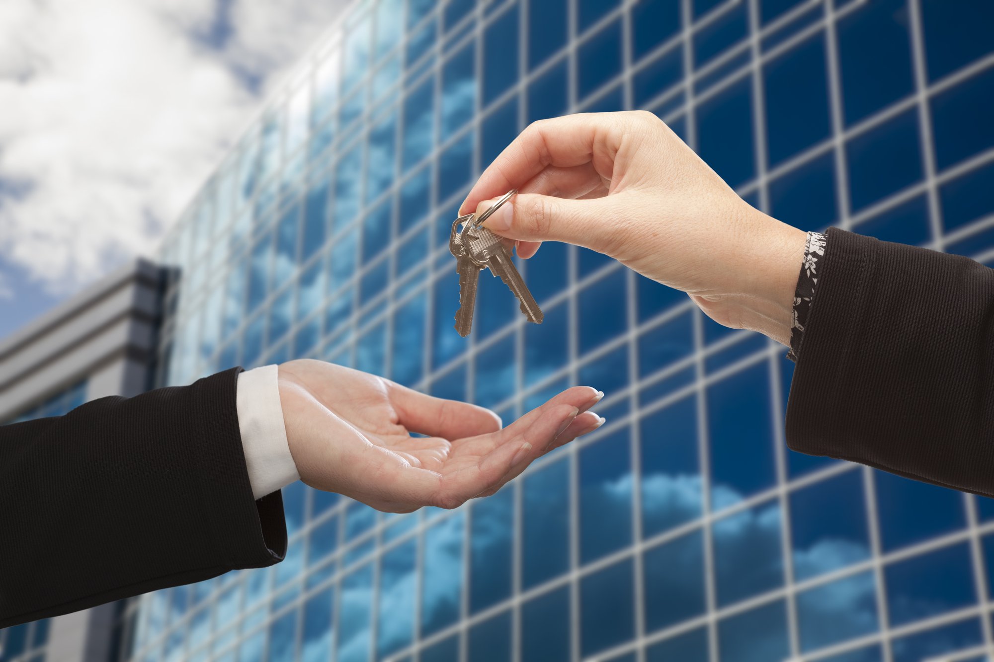 Female Handing Over the Keys to Other Woman in Front of Corporate Building.