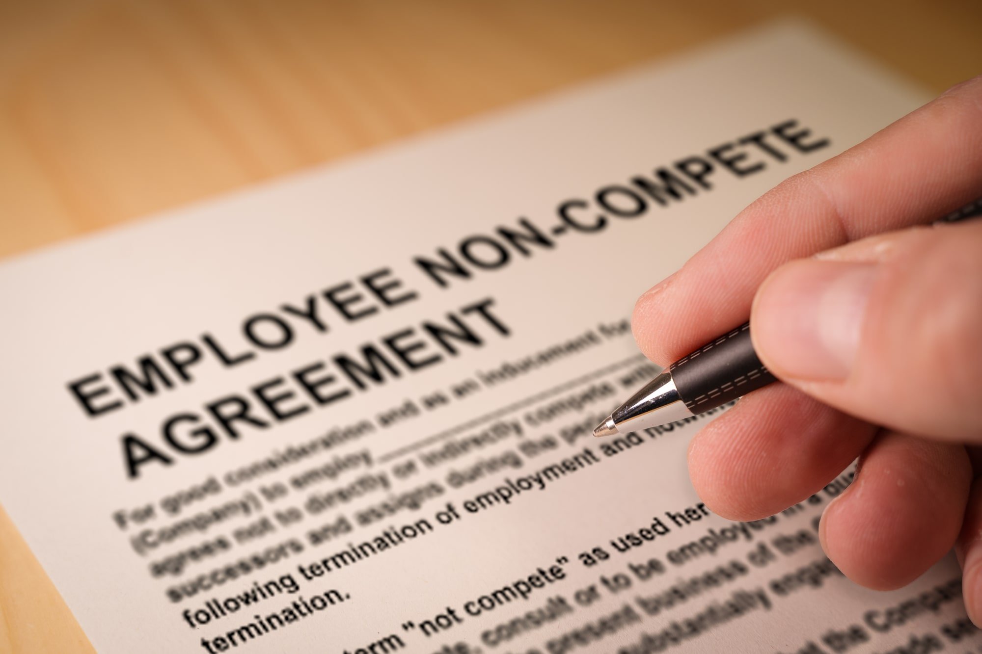 Image of a hand holding a pen signing a non-compete agreement.