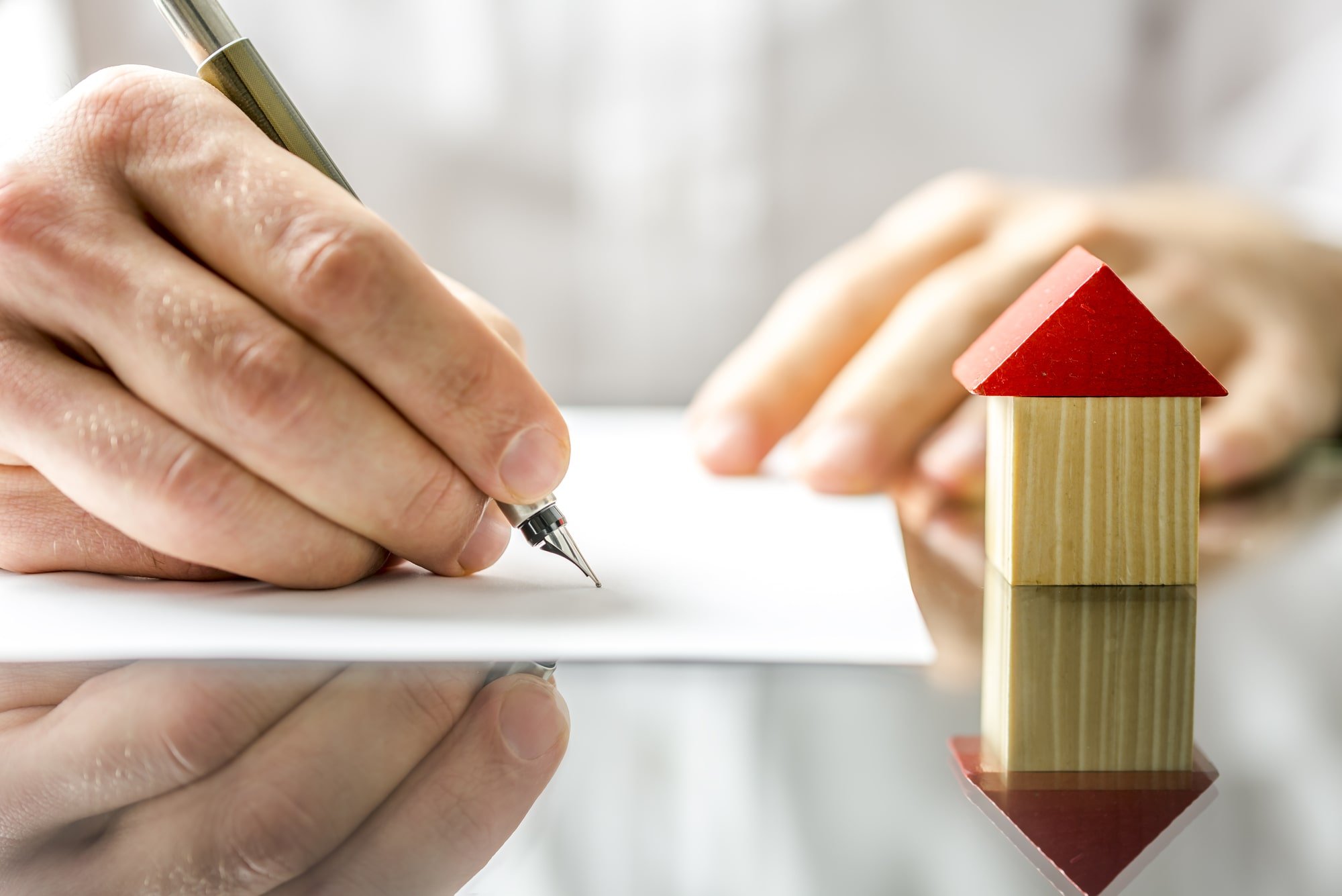 Image of a person signing a home buyer contract with a home made of blocks.