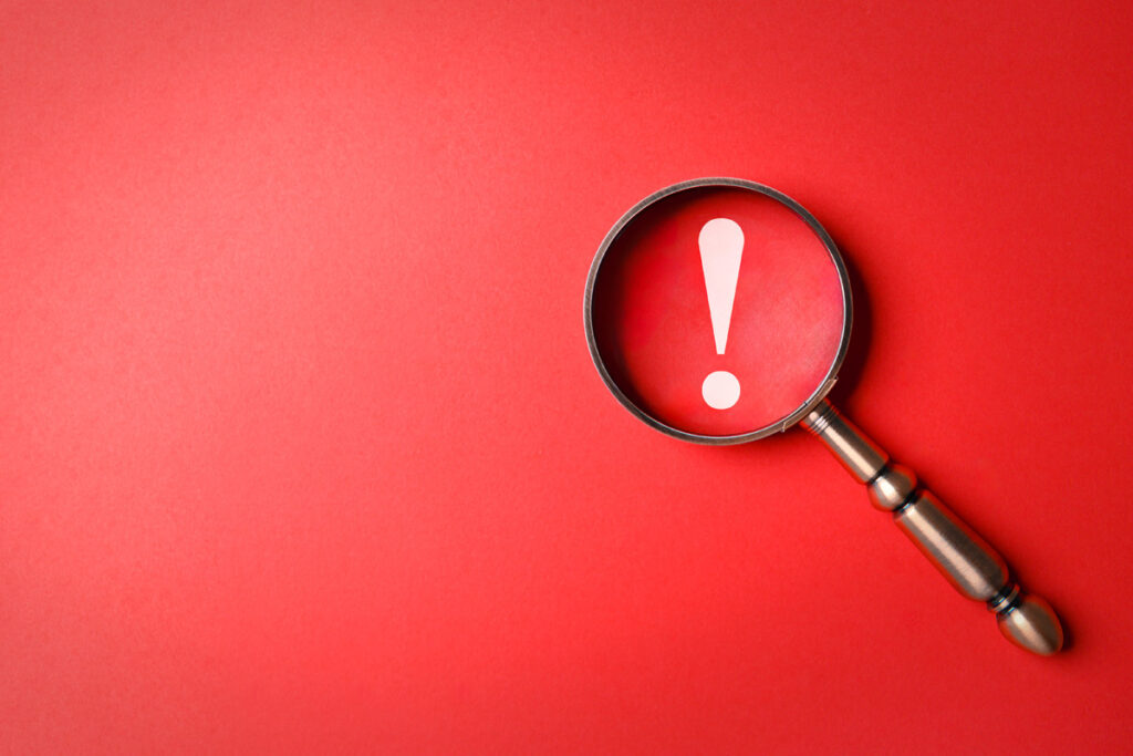 A magnifying glass zooms in on an exclamation mark and lays flat on a red background, indicating an important alert
